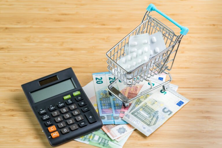 White package medicine or pills in miniature shopping cart or trolley with calculator on pile of Euro banknotes money on wood table with copy space, health care, medical or pharmacy cost concept.